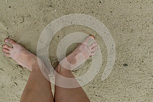 Feet naked barefoot without shoes burrow in the sand on a sandy beach, white skin