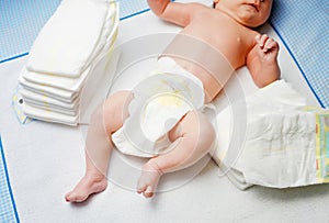 Feet of newborn baby on changing table with diapers. Cute little girl or boy two weeks old. Dry and healthy body and