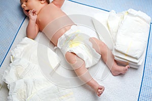 Feet of newborn baby on changing table with diapers. Cute little girl or boy two weeks old. Dry and healthy body and