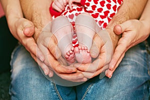 Feet of a newborn baby in the hands of parents. Happy Family concept. Mum and Dad hug their baby`s legs.