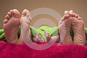 Feet of newborn baby and parents together on the bed