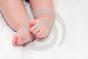 Feet newborn baby on a white bedspread. Small baby legs close up