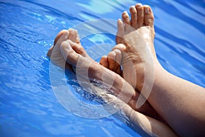 Feet paddling in clear swimming pool water.