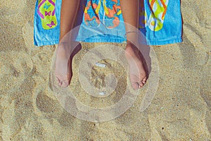 feet of a person lying on a towel on the beach, top view