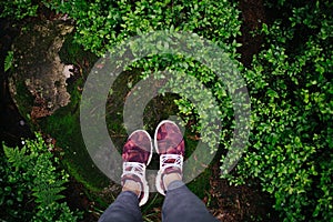 Feet in pink sneakers on the rock with green background