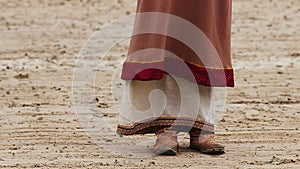 Feet of poor woman in medieval clothes begging. Pauper girl dressed in old rags