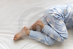 feet of preschool baby boy on blue pajama lying on white bed at home. plump legs of sleeping 3 year old caucasian child