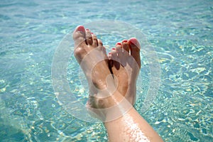Feet with red pedicure of girl on the background of sea. Girl at the resort. Female feet on sea background.