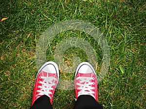 Feet in red sneakers on green grass, top view