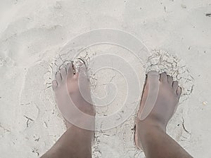 An African man standing with toes in sand on the beach.