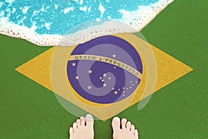 Feet on on sandy beach with flag Brazil. View from top on surf
