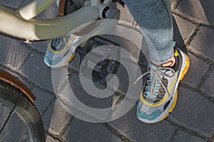Feet shod in bright sneakers are next to the bicycle