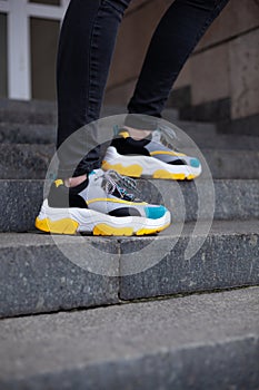 Feet shod in multi-colored sneakers of yellow, white, black and blue on the stairs