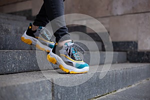 Feet shod in sneakers multi-colored yellow, white, black and blue down the stairs