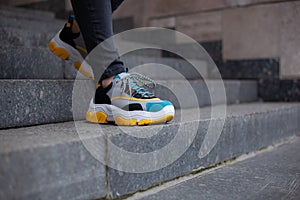 Feet  shod in sneakers multi-colored yellow, white, black and blue down the stairs