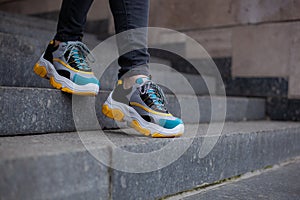 Feet  shod in sneakers multi-colored yellow, white, black and blue down the stairs