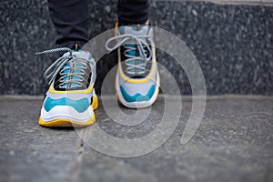 Feet  shod in sneakers multi-colored yellow, white, black and blue are placed on a wall
