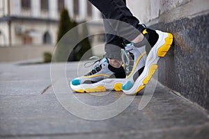 Feet shod in sneakers multi-colored yellow, white, black and blue are placed on a wall