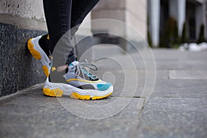 Feet  shod in sneakers multi-colored yellow, white, black and blue are placed on a wall