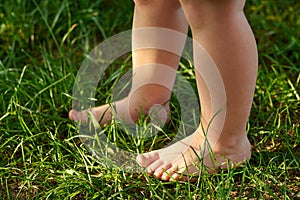 The feet of a small child on the grass, walking on bumps