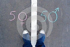 Feet in sneakers between the male and female symbol on the asphalt