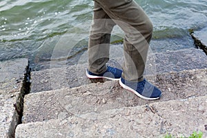 Feet in sneakers stand on steps above water