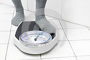 Feet in socks stepping on a personal scale on the tiled bathroom floor to measure the body weight, copy space
