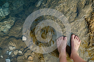 feet standing by the edge of a clear, bubbling spring
