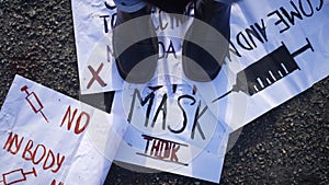 Feet stomping on anti-vax placards on the ground. Unrecognizable activist stepping on anti-vaccination banners outdoors.