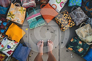feet surrounded by assorted fabric totes on a sidewalk