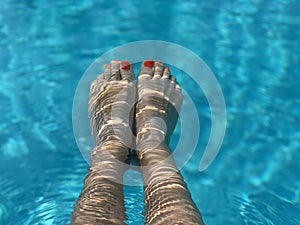 Feet in the swimming pool. Relax, vacation, summer. Red nails, suntanned skin, turquoise water. Sunlight dancing in the water.