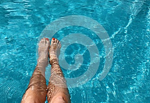 Feet in the swimming pool. Relax, vacation, summer. Red nails, suntanned skin, turquoise water. Sunlight dancing in the water.