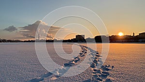 Feet traces with winter industrial landscape over the snow covered city at sunset