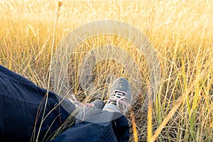 Feet of a traveler in gray sneakers. A tired man rests in a field in autumn at sunset