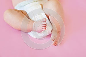 Feet of a two months old baby wearing diapers lying on the bed at home