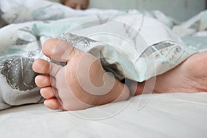 Feet under a light blanket on the bed. Concept of health