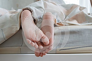 Feet under a light blanket on the bed, soft focus background