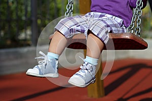 Feet of unrecognizable baby swinging on playground