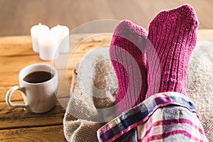 Feet up in cozy woolly pink socks with cup of tea and candles