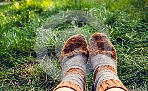 Feet in warm woolen socks. Knitted wool socks. Feet in socks on the background of green grass. Autumn concept, travel