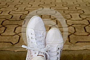 Feet in white sneakers relaxing on the garden`s concrete block pavement