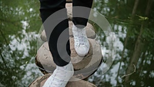 Feet in white sneakers walking on stones path above pond