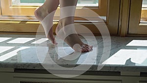 Feet on a windowsill. Young woman barefoot circling and dancing in room.