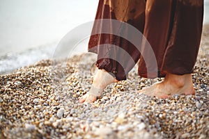 Feet of a woman in brown trousers in pebbles on the seashore