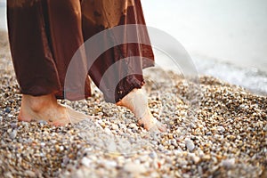 Feet of a woman in brown trousers in pebbles on the seashore