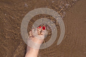 Feet of woman with nails painted red on the sand of the sea