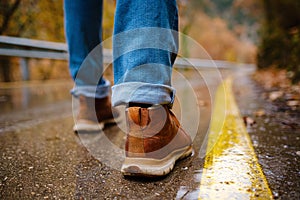 Feet of a woman walking along asphalt road in autumn forest