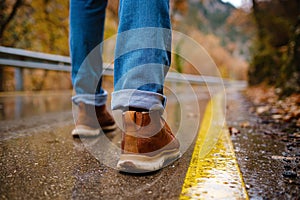 feet of a woman walking along asphalt road in autumn forest