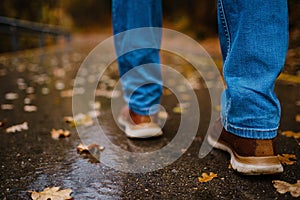 feet of a woman walking along asphalt road in autumn forest