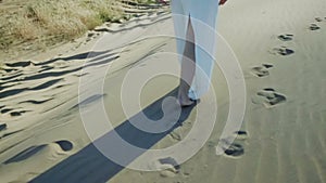 Feet of woman walking on beach dunes in white dress while sun drops shadow